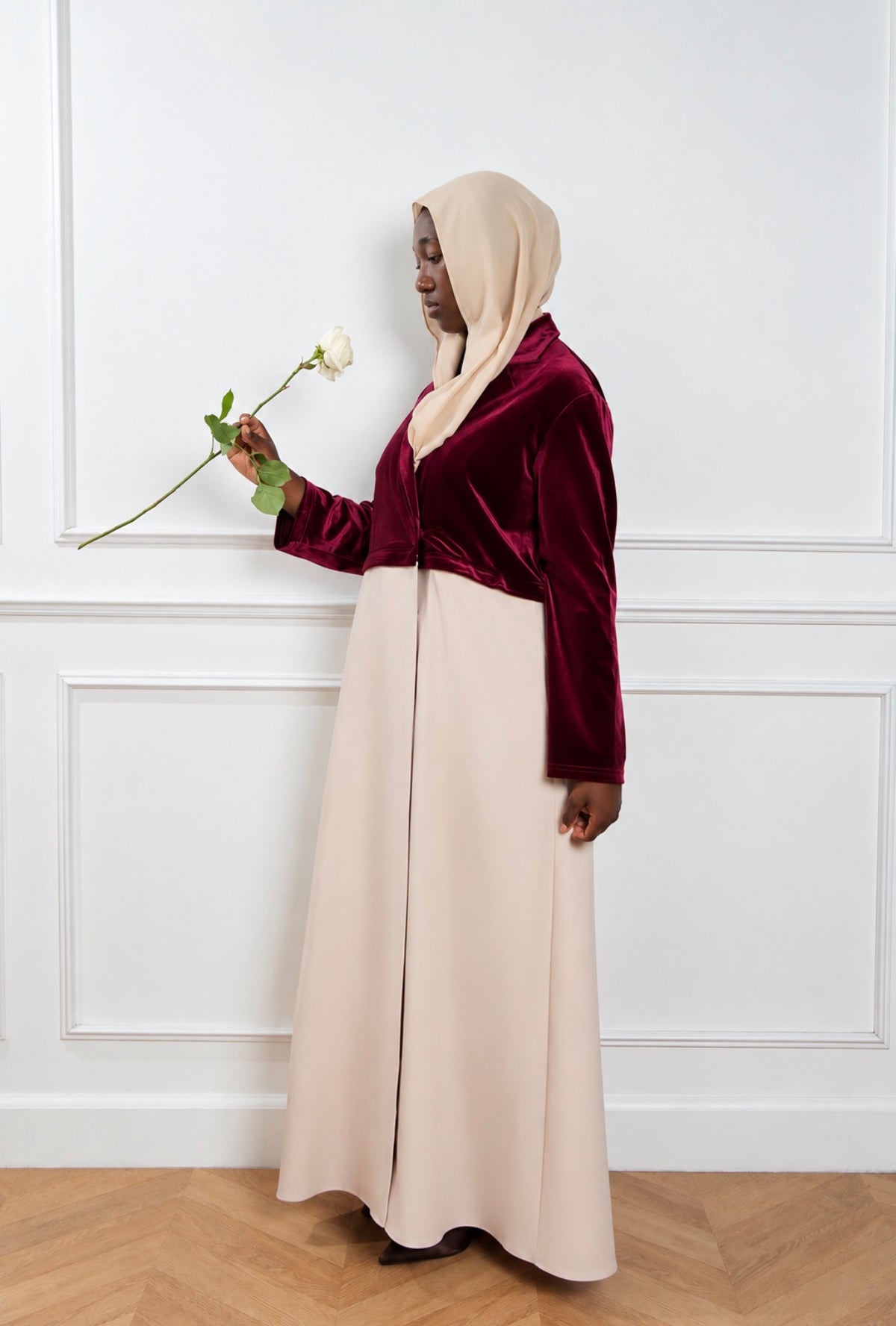 Abaya Opéra bordeaux et beige, portée de trois quarts avec une rose.